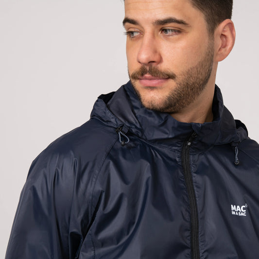 Man wearing a navy waterproof jacket with a integrated hood and a visible brand logo on a plain background