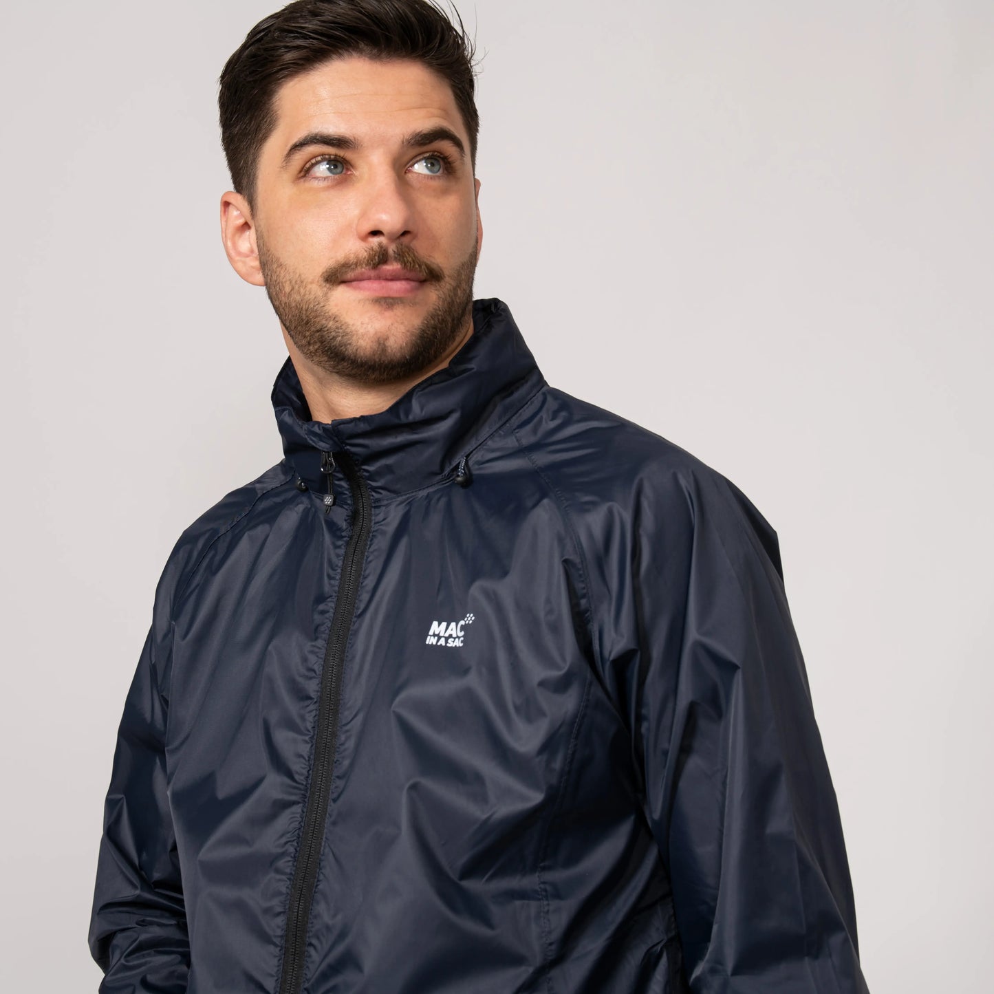 Man wearing a navy waterproof jacket with the hood tucked in while showing fully taped seams and a brand logo on a light gray background