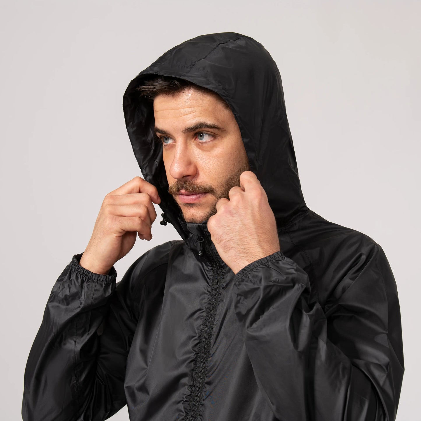 Man wearing a black waterproof and windproof rain jacket with the hood over his head against a plain background