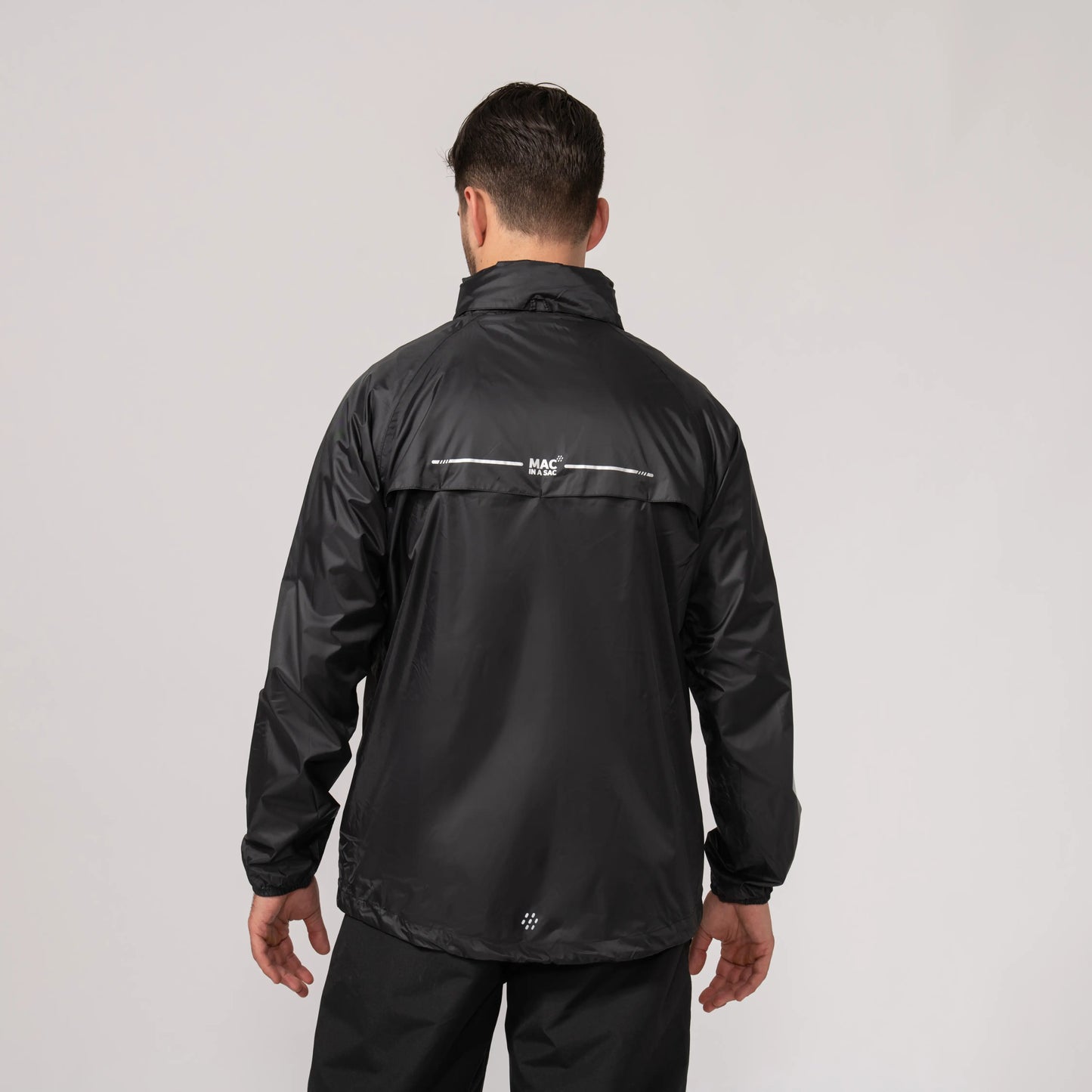 Person wearing a black waterproof and windproof rain jacket showing the length of the back with a visible brand logo on a light gray background