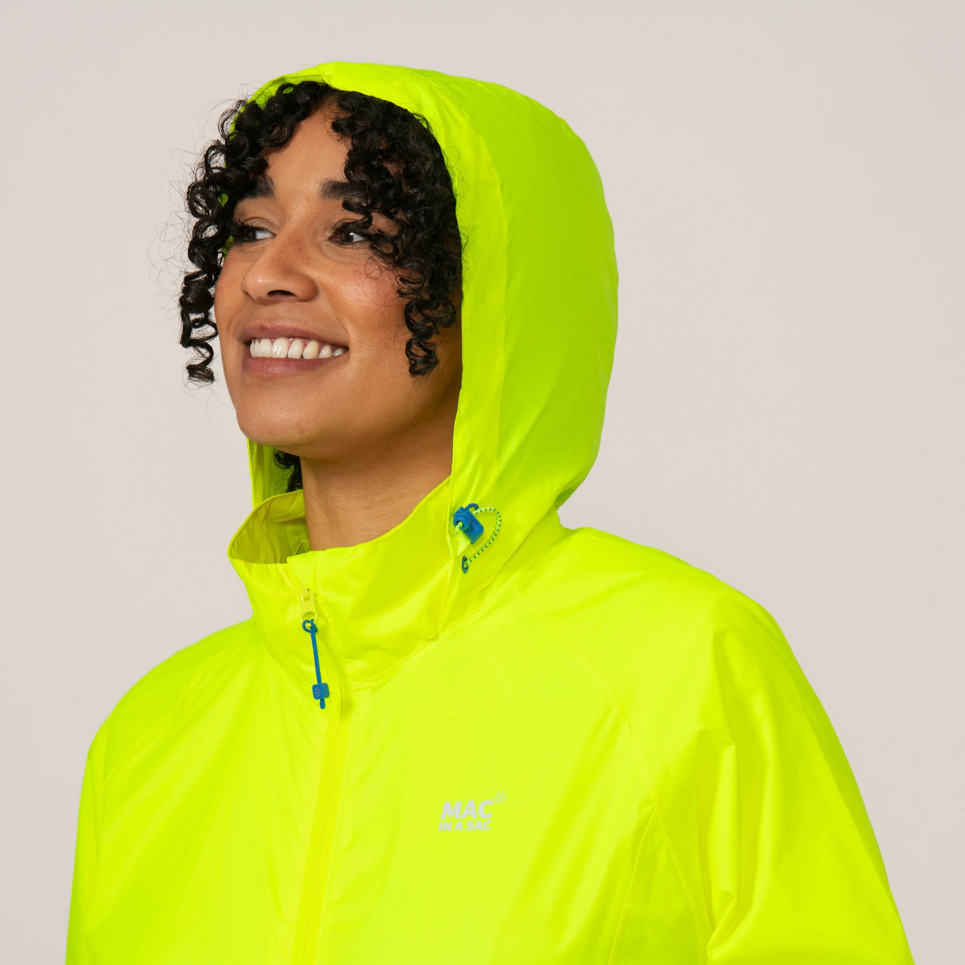 Person wearing a bright neon yellow rain jacket with a hood over her head on a plain background