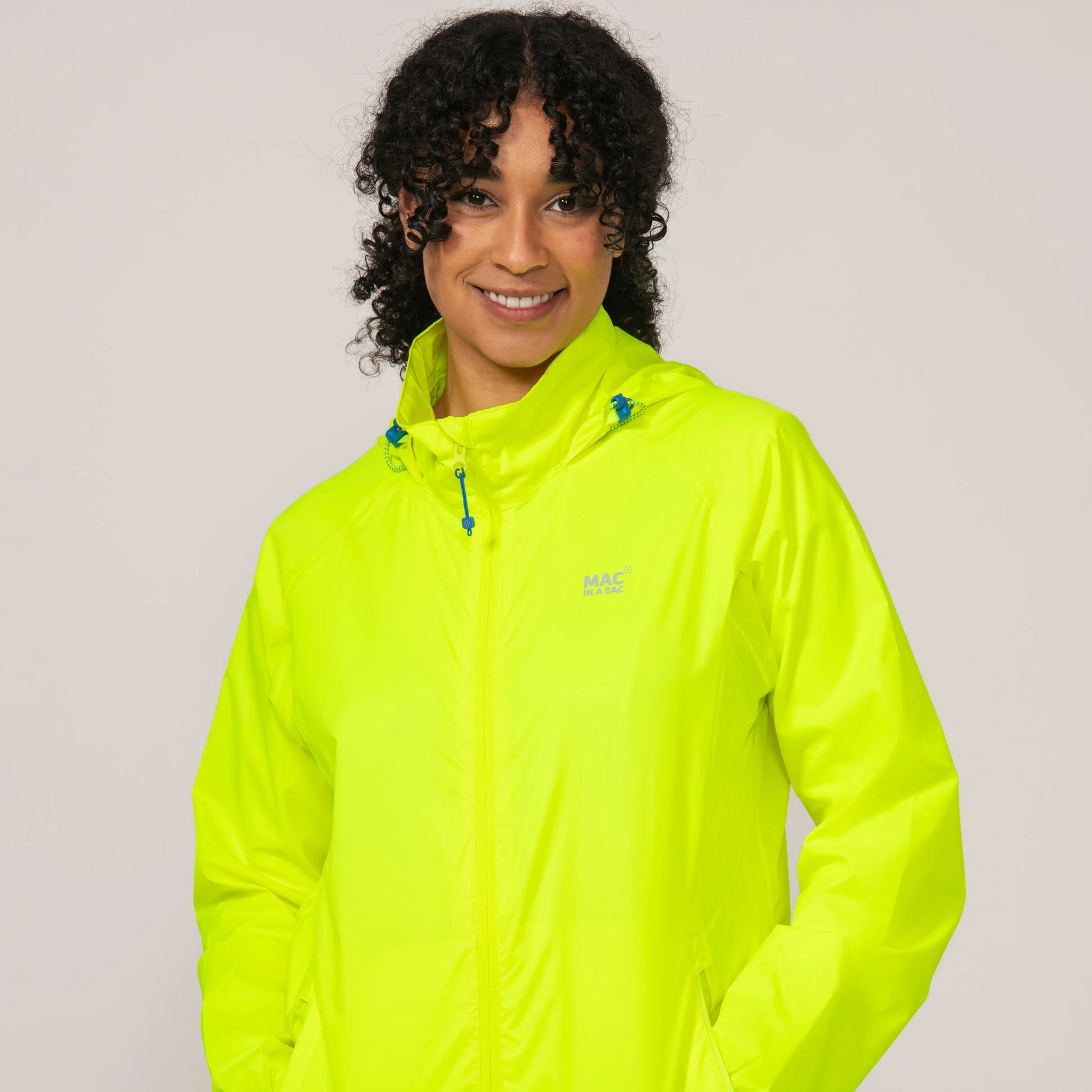 Person wearing a bright neon yellow waterproof and windproof jacket close up with a visible brand logo on a plain background
