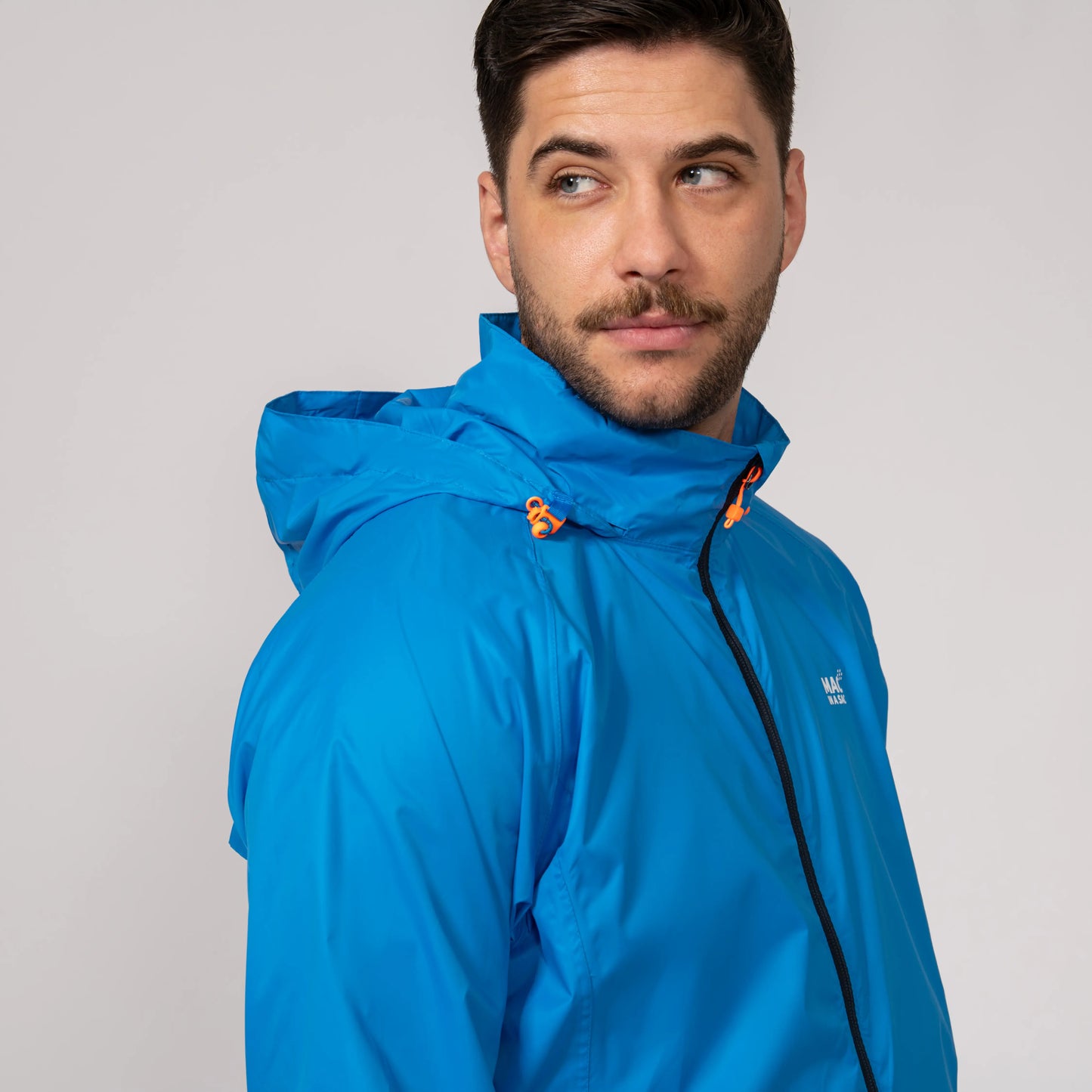 Man wearing a blue waterproof and windproof jacket showing the integrated hood with a brand logo on a gray background