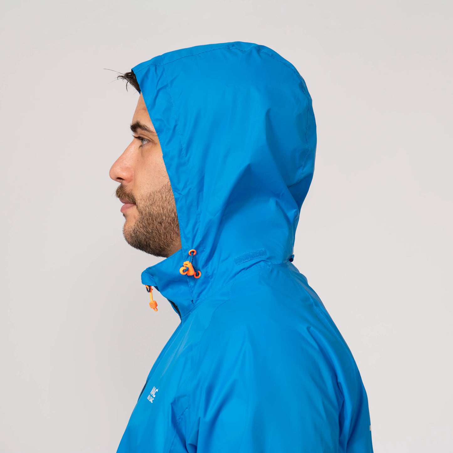 Person wearing a blue waterproof jacket with a hood displayed from the side on a light gray background