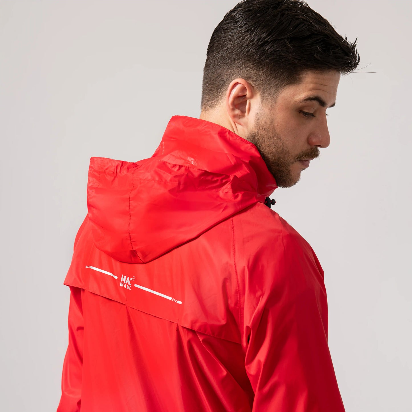 Man wearing a red waterproof and windproof jacket showing the integrated hood with a brand logo on a light gray background