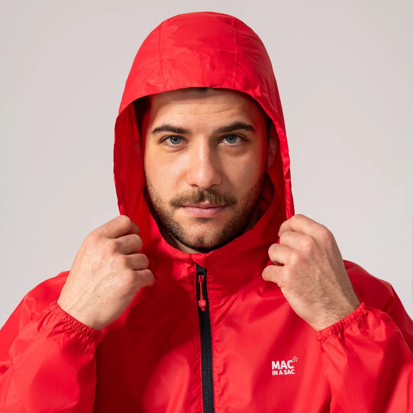 Man wearing a red waterproof and windproof jacket with a hood over his head, featuring the MAC In A SAC brand logo.