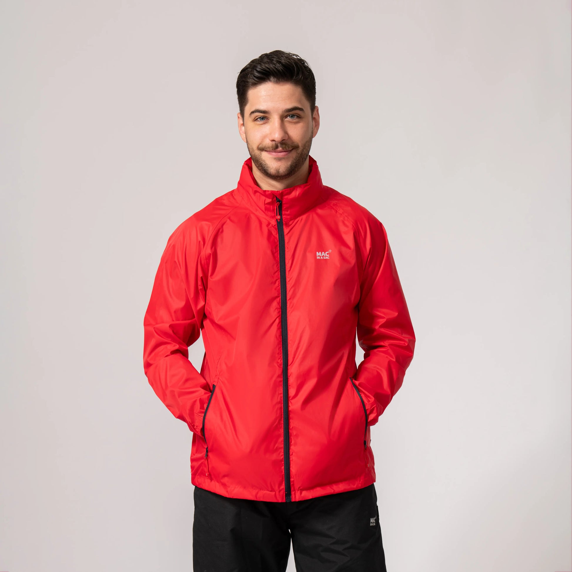 Man wearing a red waterproof and windproof jacket with his hands in his pockets with a brand logo on a light gray background
