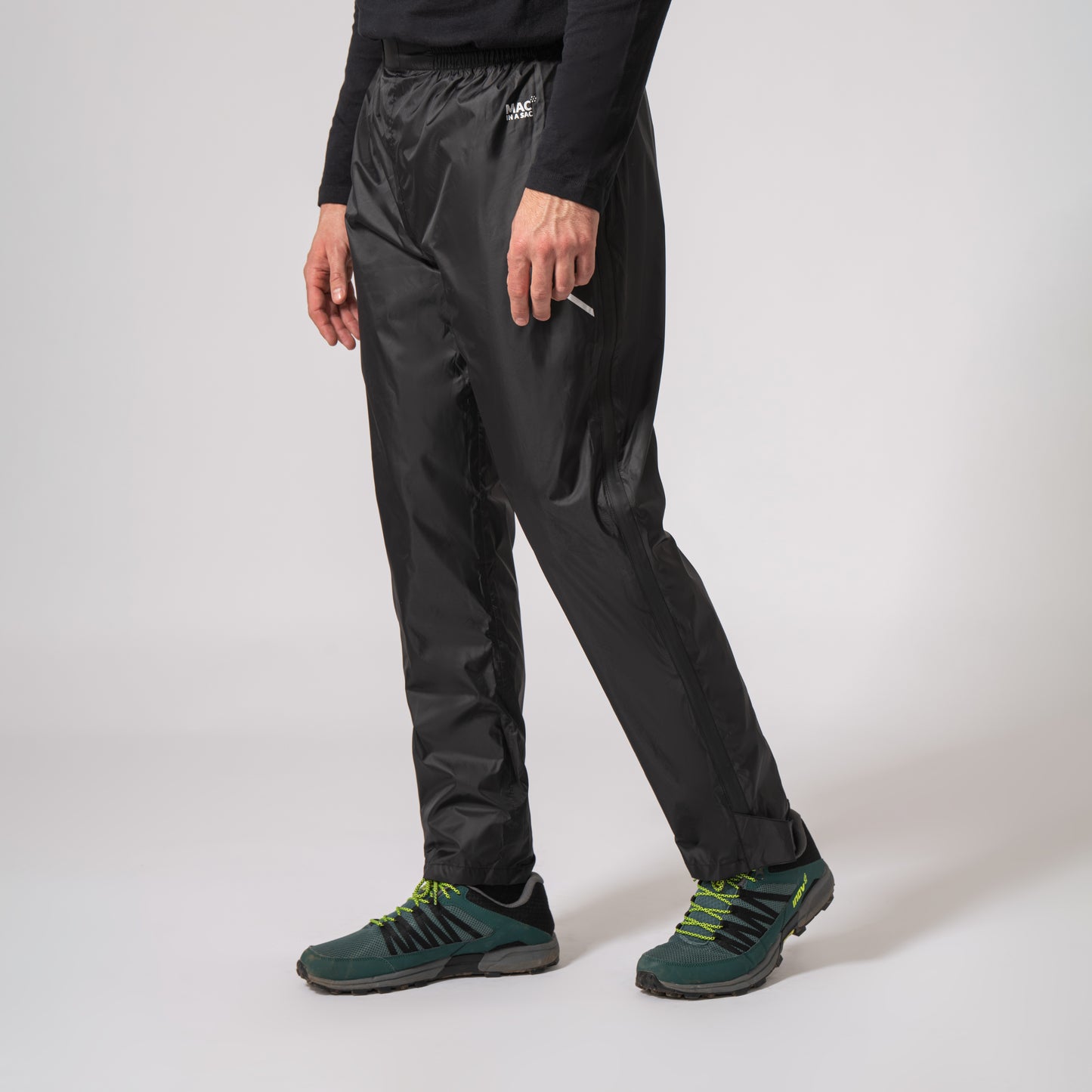 black waterproof overtrousers walking to the left with a white background