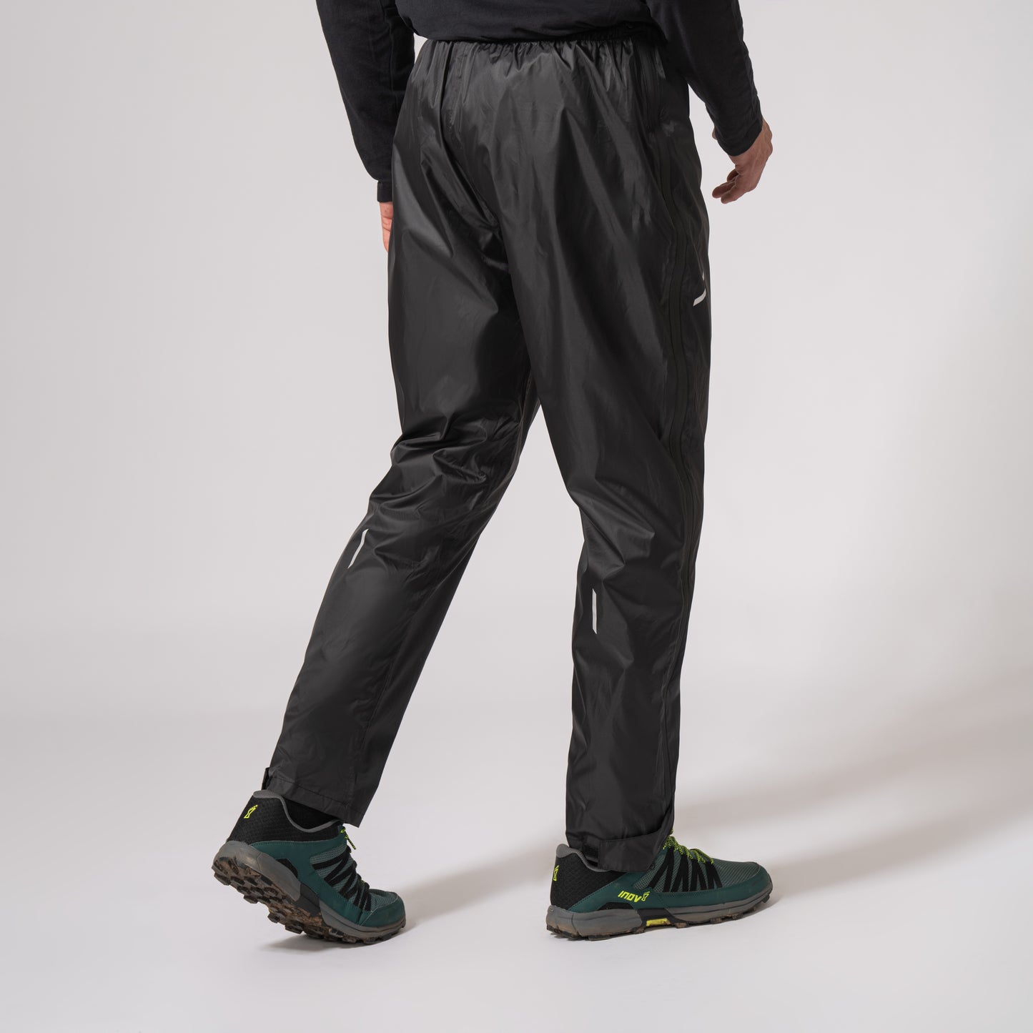 Black waterproof overtrousers walking to the right with a white background