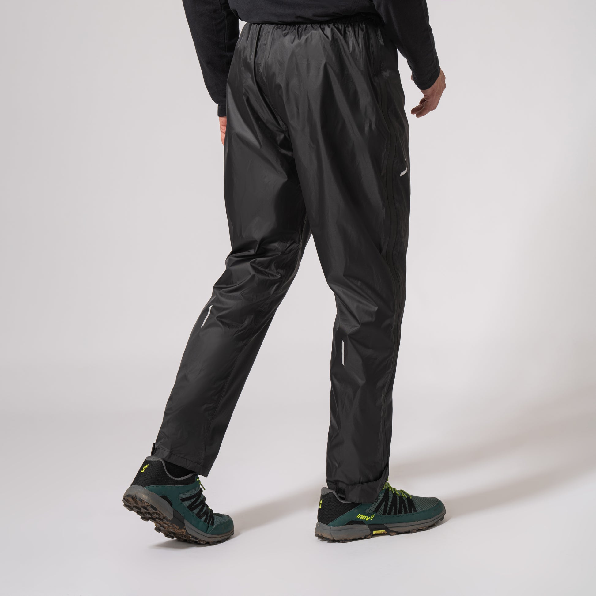 Black waterproof overtrousers walking to the right with a white background